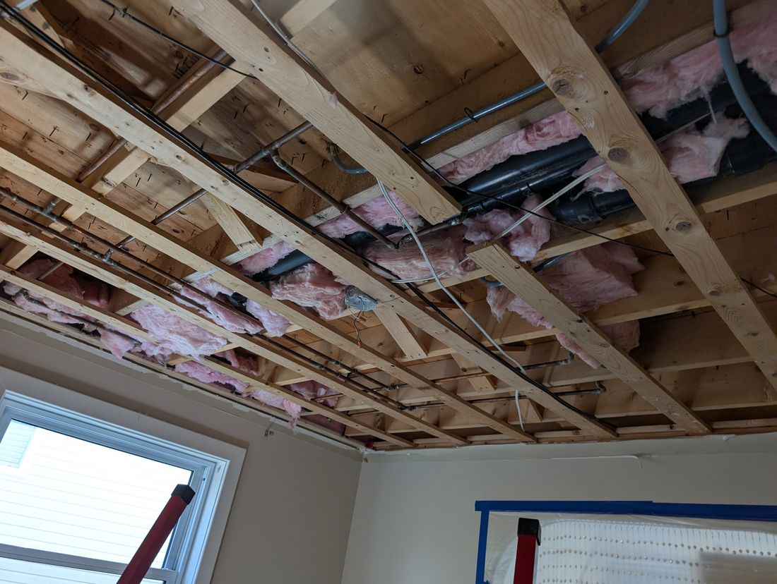 A ceiling stripped back to the joists with insulation and wiring exposed.